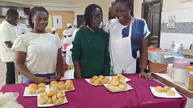 Three trainees smiling behind trays of bread rolls they baked