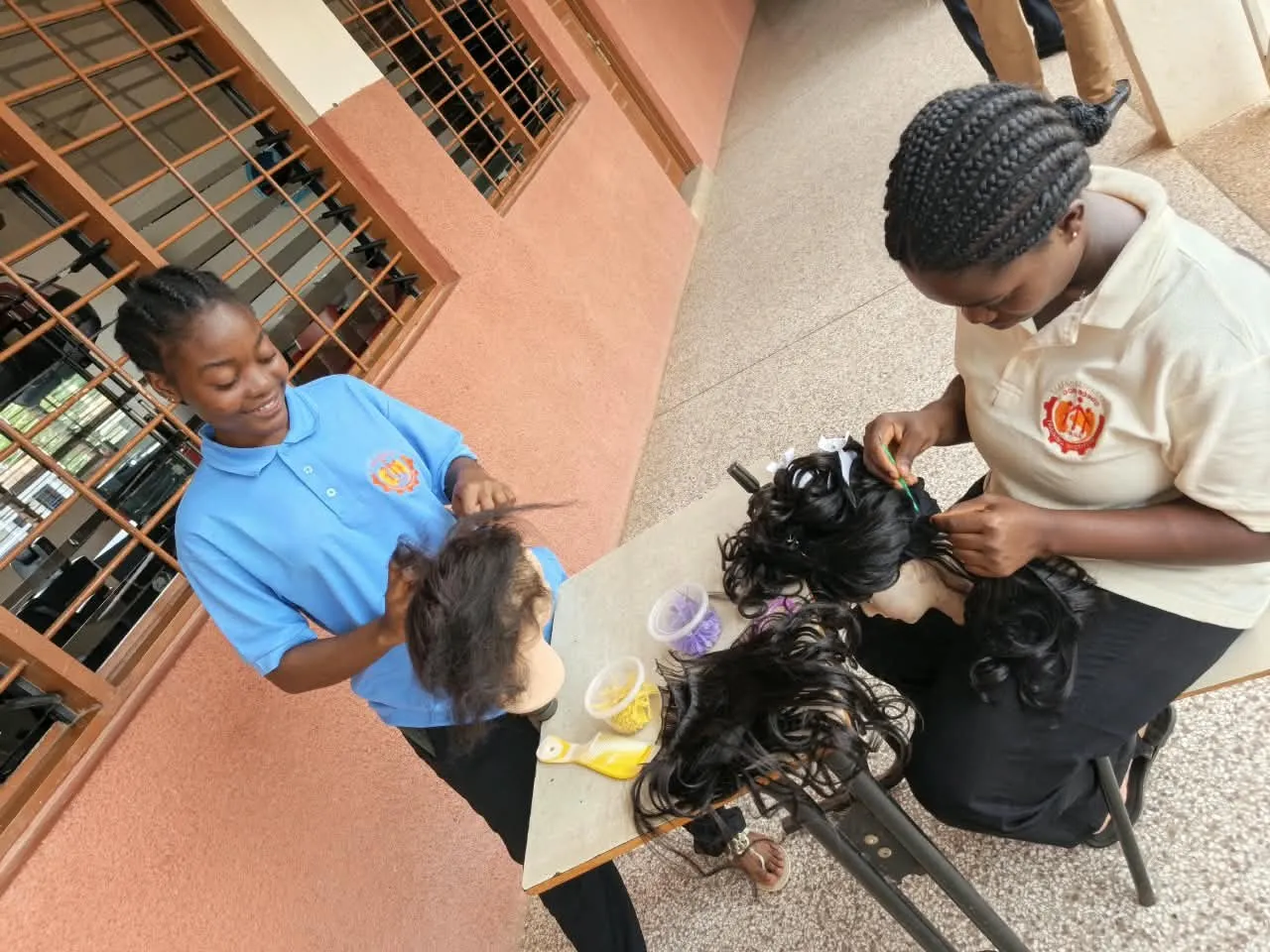 Two cosmetology trainees smiling as they make wigs on mannequin heads